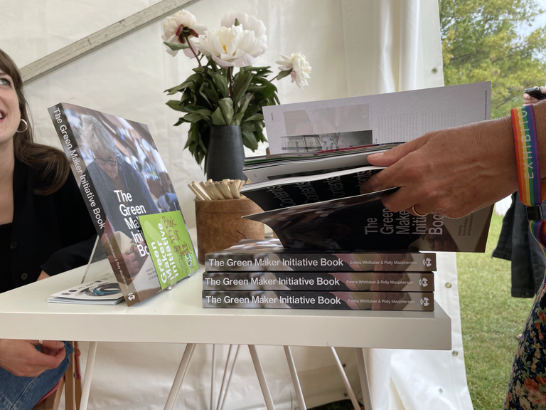 Picture of a stack of the Green Maker Initiative book. Someone's hand is holding one copy open above the stack.