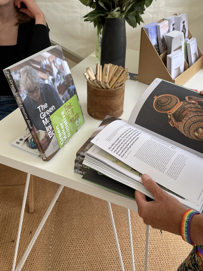 Picture of a double spread of the Green Maker Initiative book on a table with another GMI book on a stand and a pen holder full of carpenter's pencils
