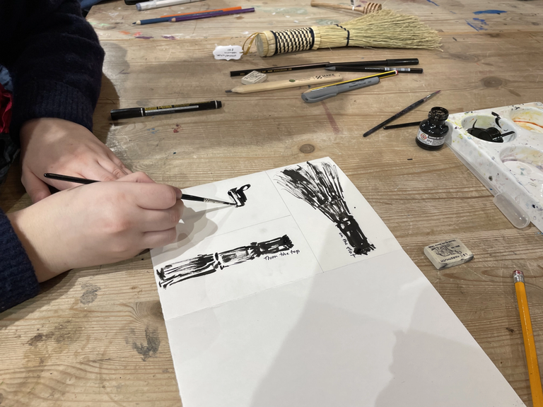 Hands holding a brush drawing a handmade straw cleaning yellow brush with black ink