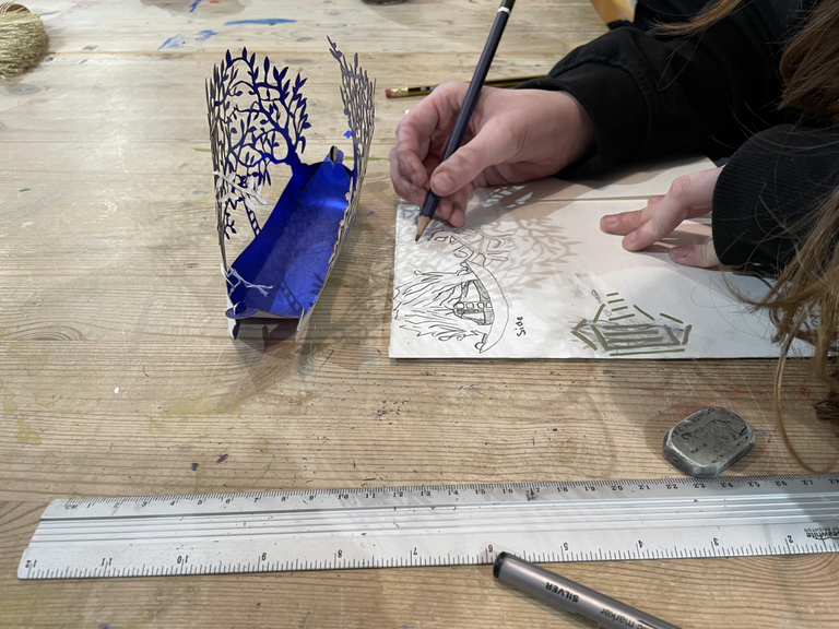 Hand holding a pencil drawing a 3D papercut tree